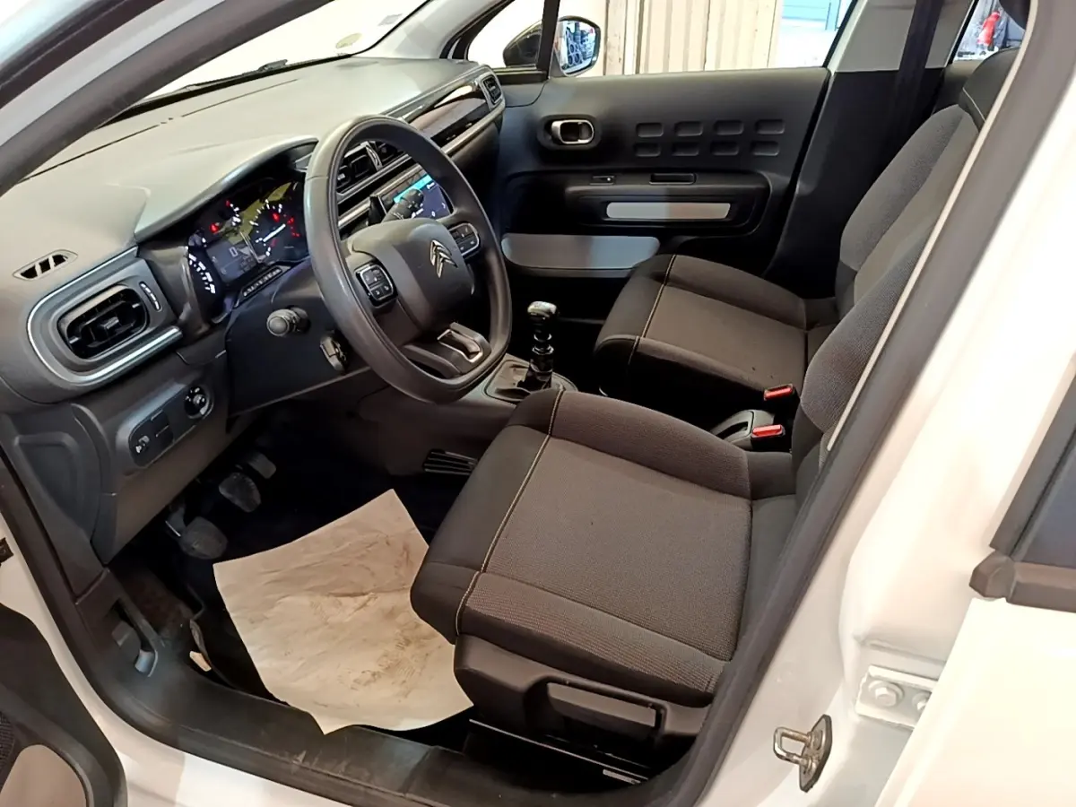 Intérieur avant droit d'une Citroën C3 blanche 2022, volant multifonctions, sièges tissu noirs et levier de vitesse manuel.