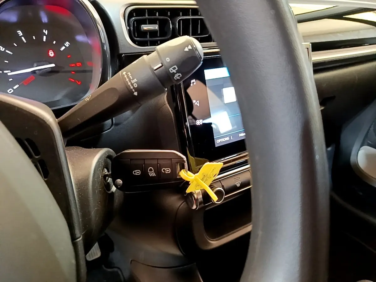 Gros plan sur le volant et le tableau de bord noir de la Citroën C3 blanche, avec la clé insérée et l'écran tactile allumé.