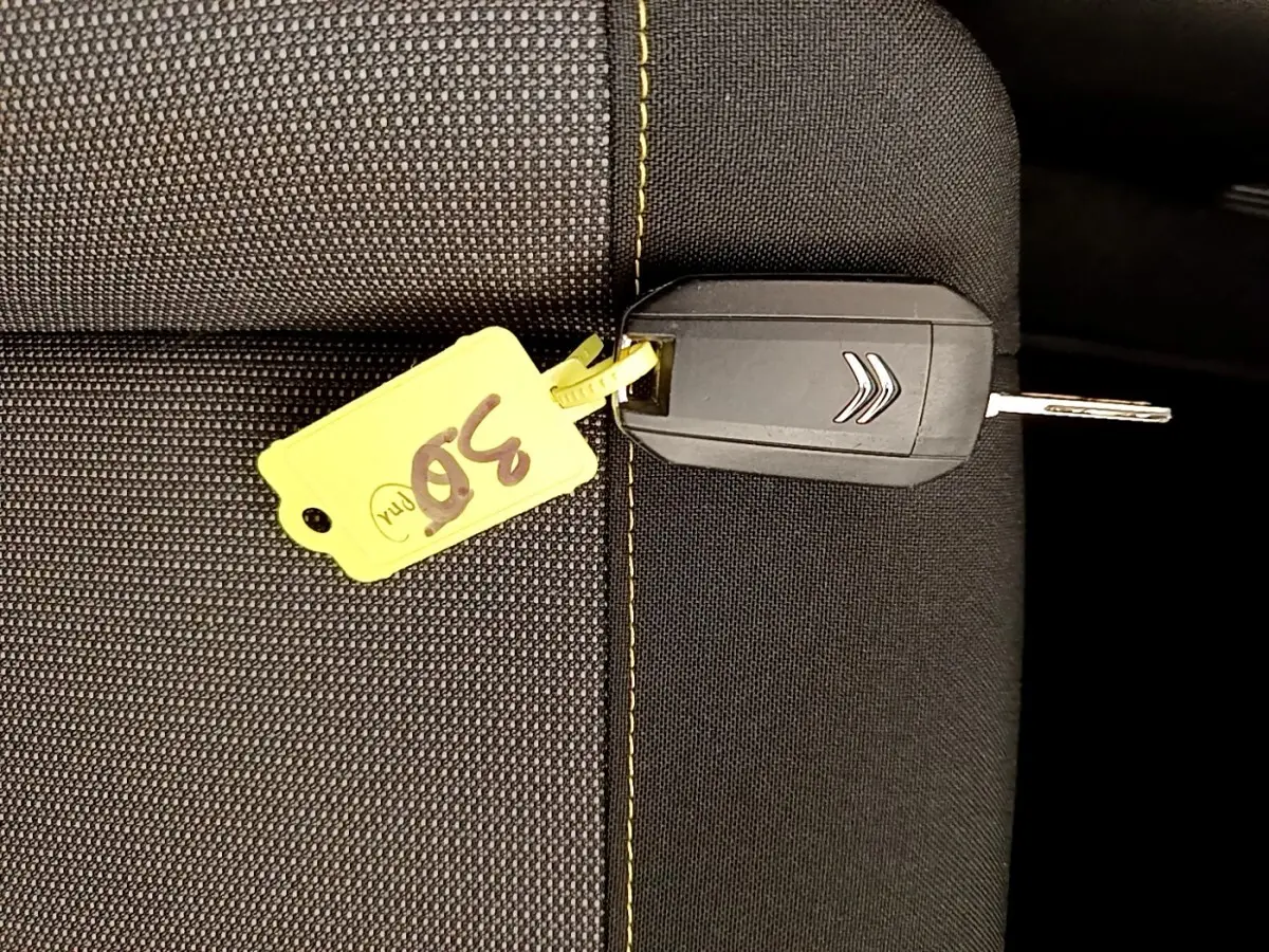 Clé de voiture Citroën posée sur un siège en tissu noir avec surpiqûres jaunes, étiquette jaune numérotée 30.