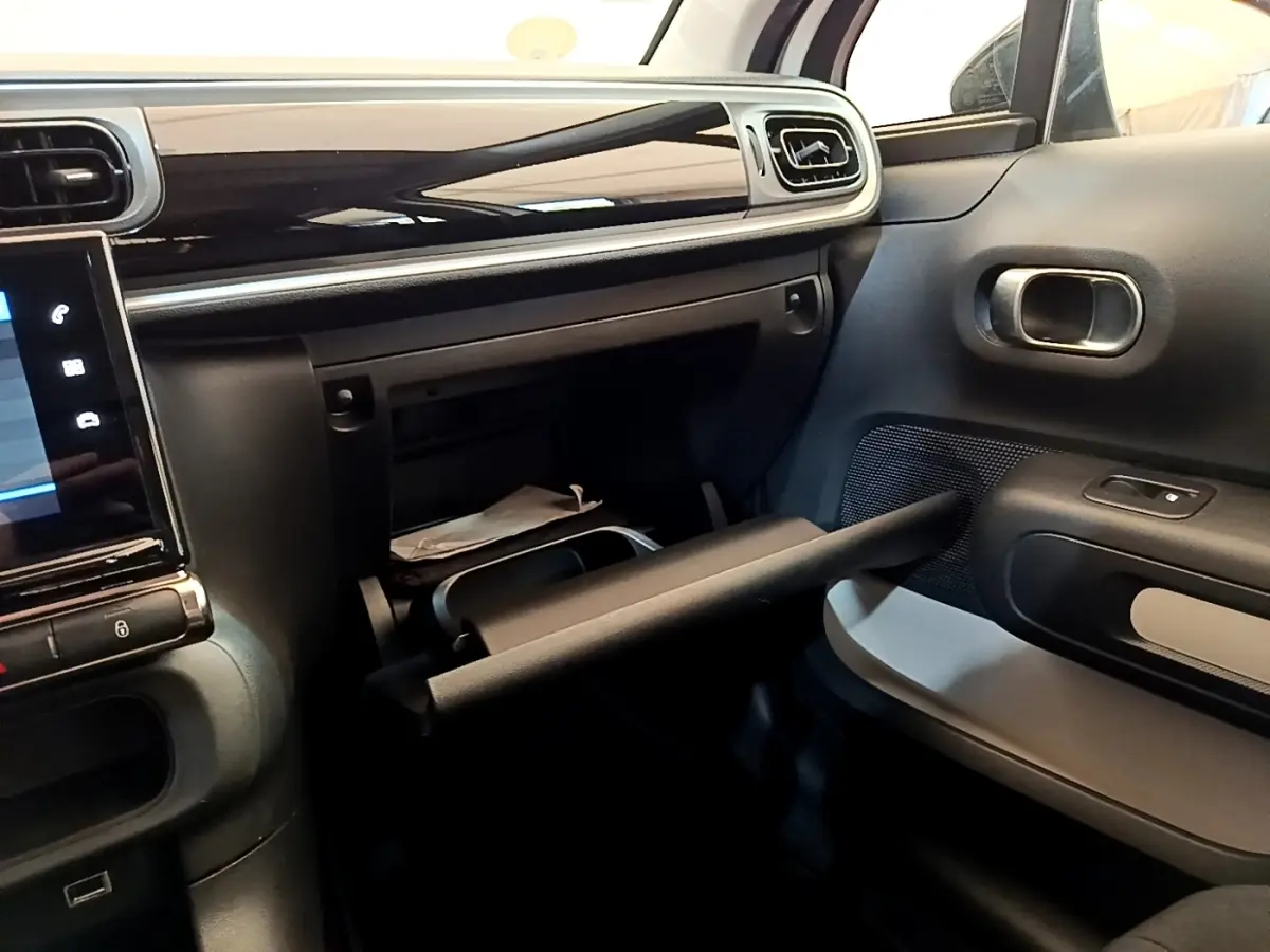 Intérieur de la Citroën C3 blanc, vue côté passager avec boîte à gants ouverte et tableau de bord noir brillant.