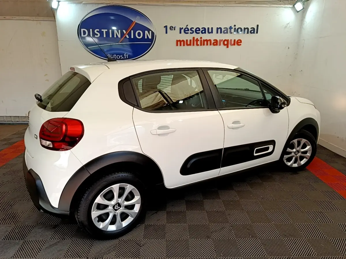 Vue latérale droite d'une Citroën C3 blanche 2022 avec protections noires sur les portières dans un showroom.