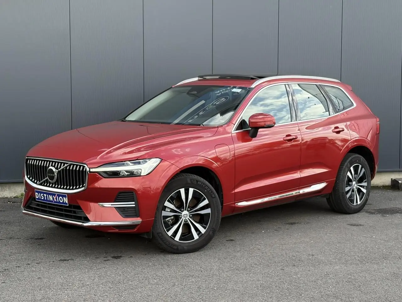 Volvo XC60 T6 AWD PHEV rouge Fusion en 3/4 avant droit, jantes alliage et toit ouvrant panoramique visibles.