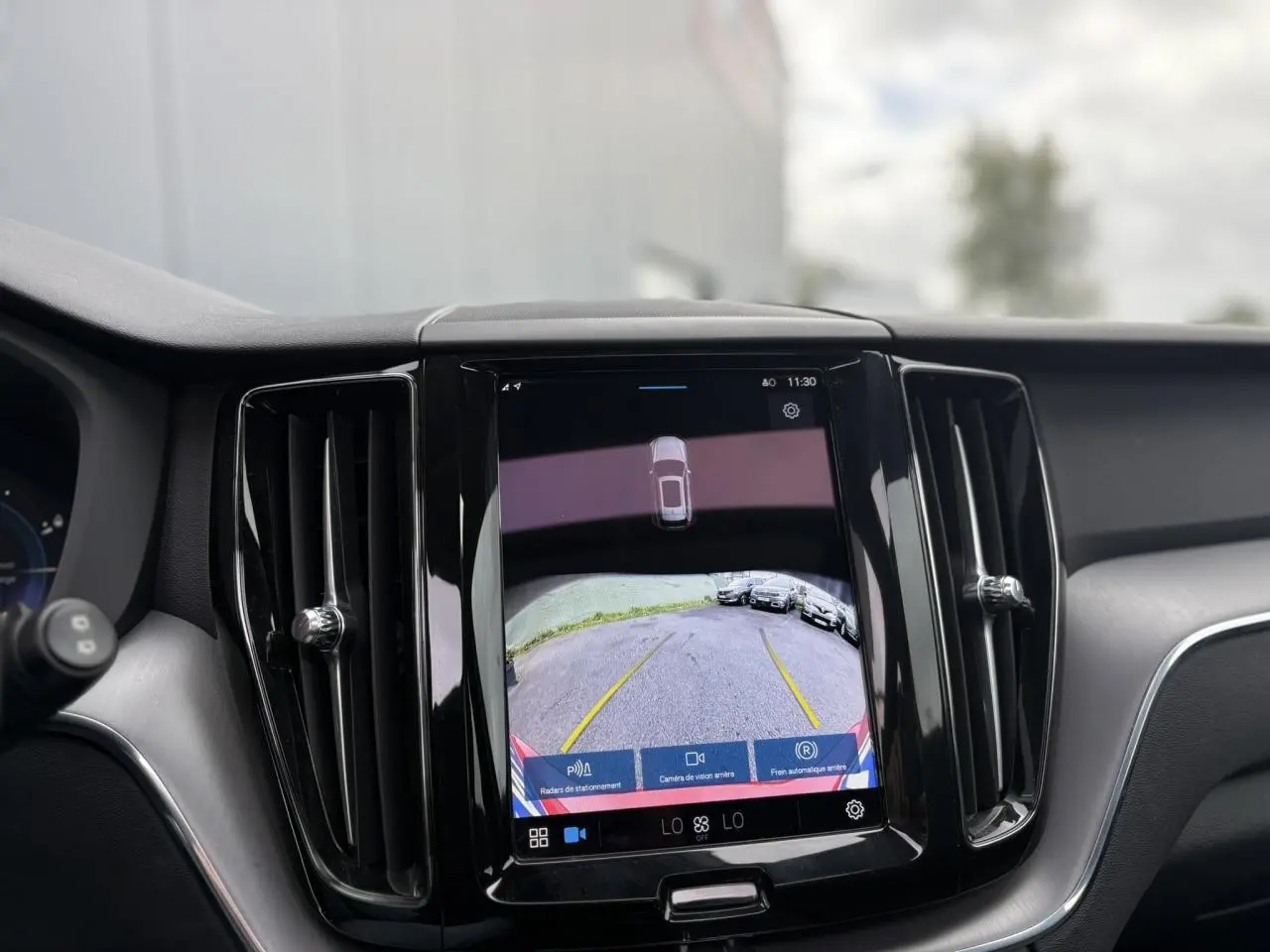 Vue intérieure du tableau de bord du Volvo XC60 2024 avec écran tactile affichant la caméra de recul.