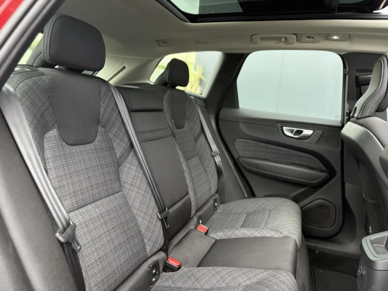 Vue intérieure arrière du Volvo XC60 2024, sièges en tissu gris à motif tartan avec ceinture de sécurité noire.