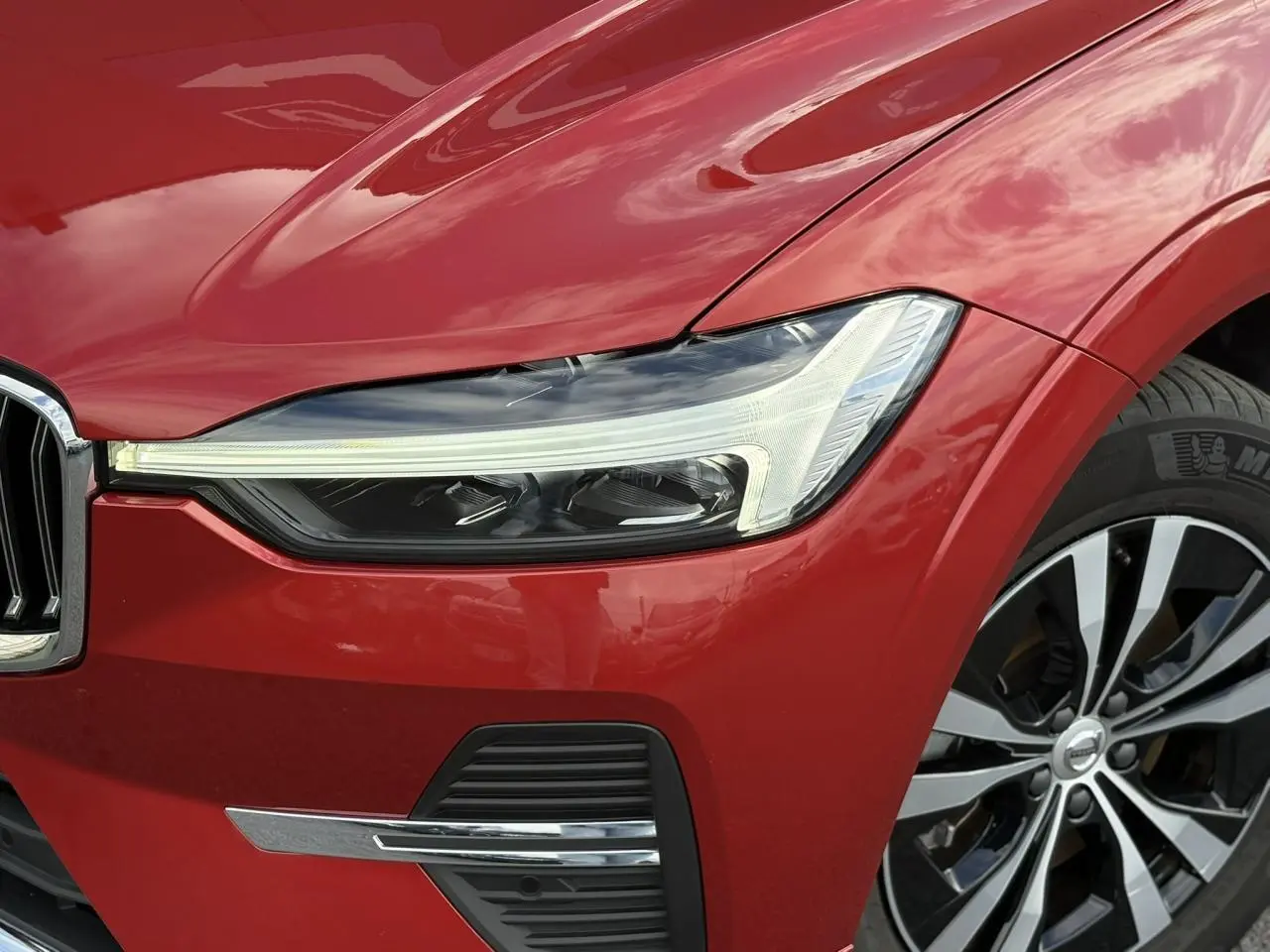 Gros plan sur l'avant droit du Volvo XC60 rouge Fusion 2024, mettant en valeur le phare LED et la jante alliage.