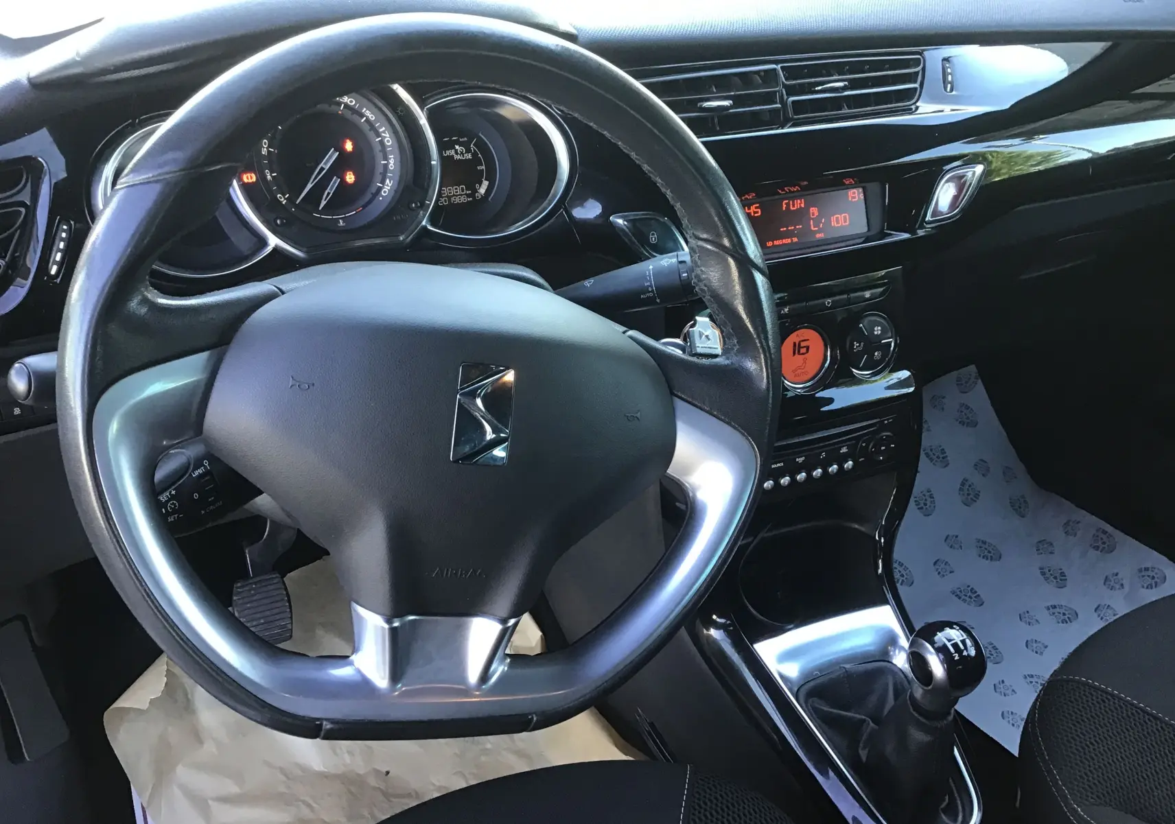 Vue intérieure centrée sur le volant cuir et tableau de bord noir brillant de la Citroën DS3 gris clair métal de 2013.