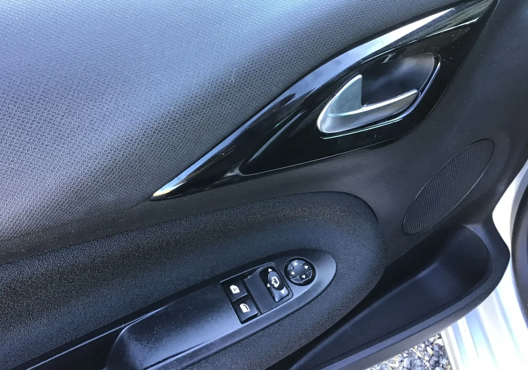 Gros plan sur la porte côté conducteur d'une Citroën DS3 gris clair, montrant la poignée intérieure et les commandes des vitres.