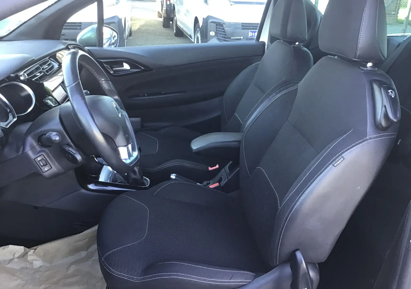 Vue intérieure côté conducteur de la Citroën DS3 2013, sièges noirs avec surpiqûres blanches et volant cuir.