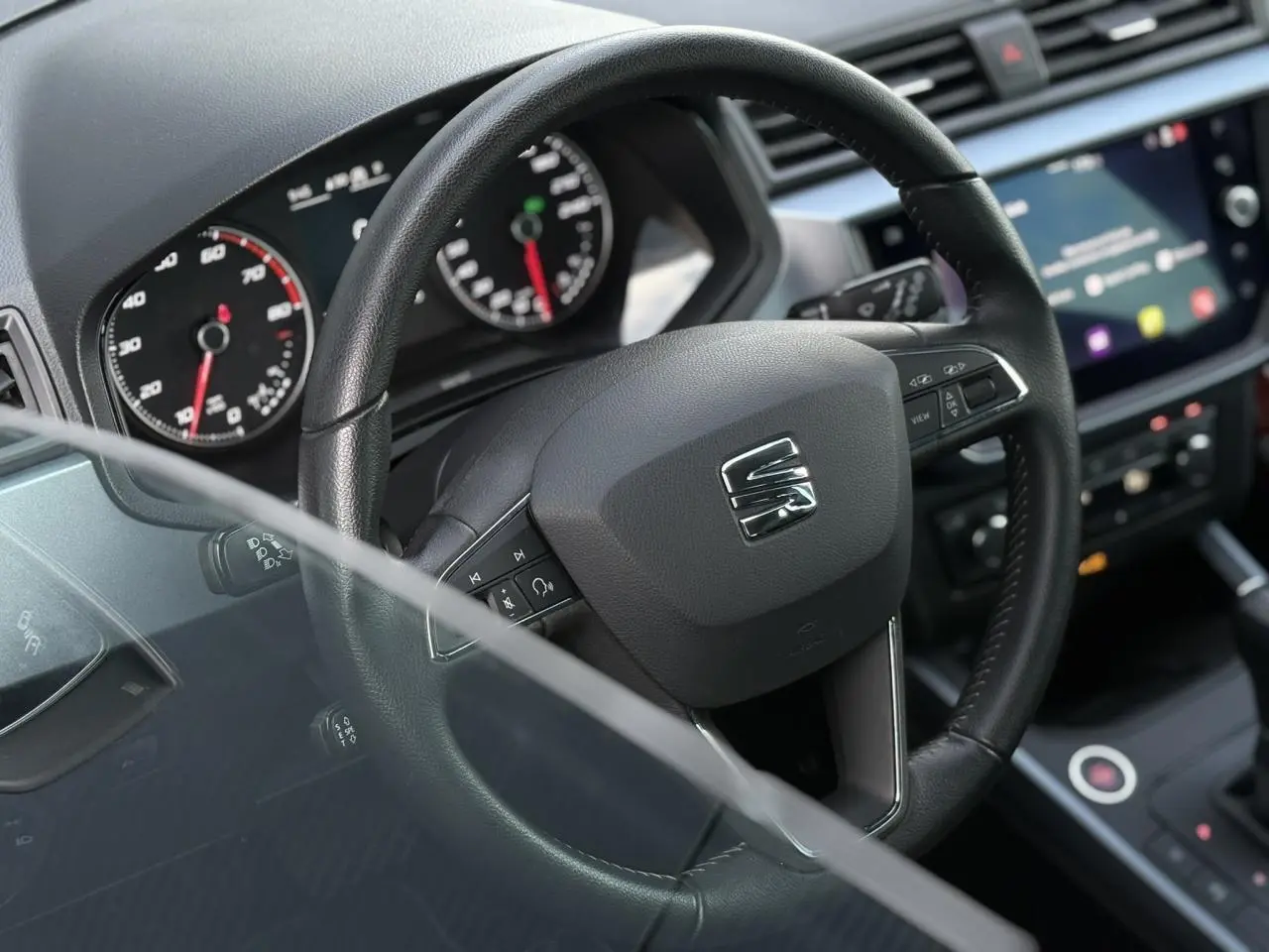 Vue rapprochée du volant en cuir noir d'une SEAT Arona 2020, avec tableau de bord et écran tactile en arrière-plan.