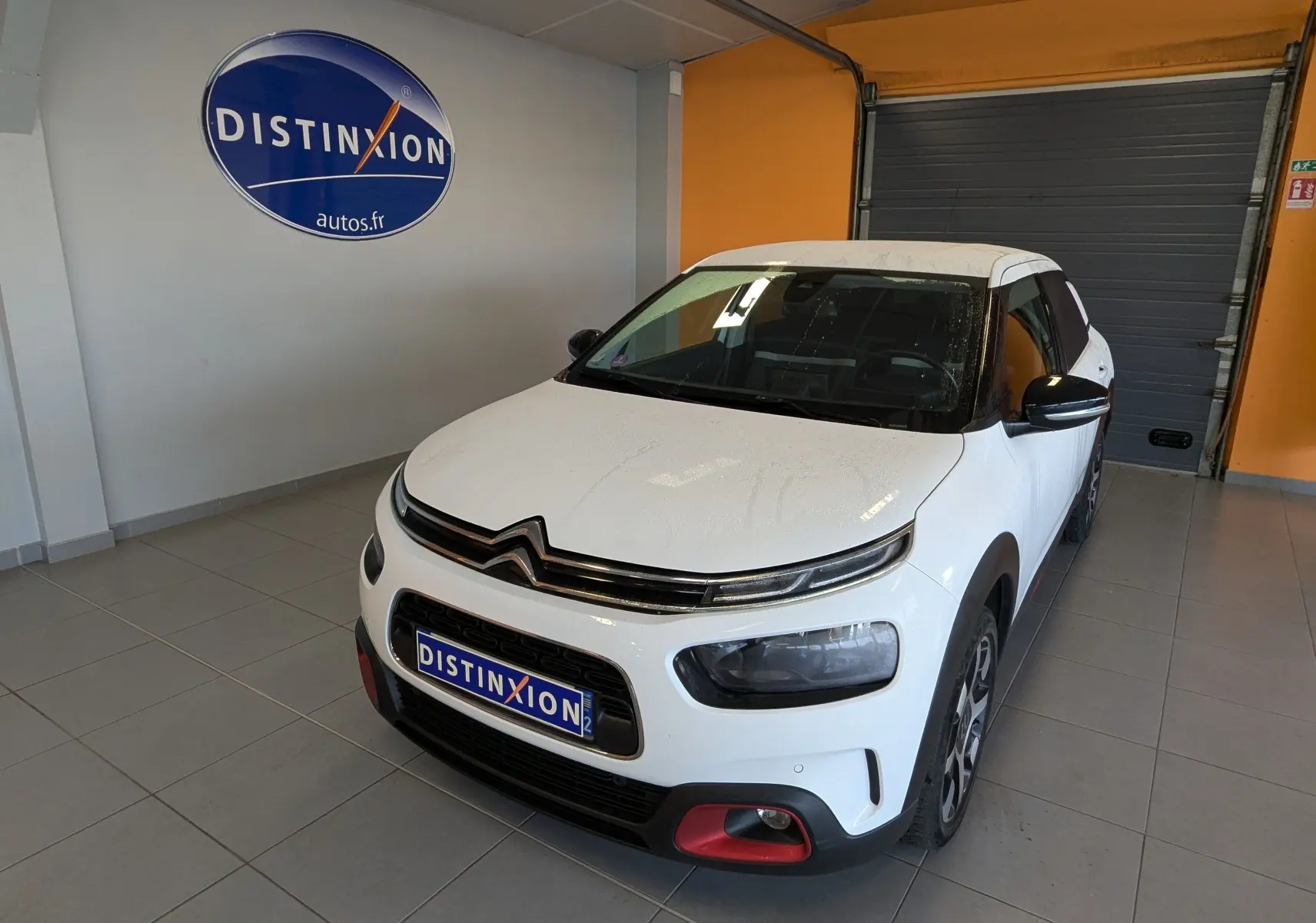 Citroën C4 Cactus blanc vue 3/4 avant droit en intérieur, avec détails rouges sur le pare-chocs et jantes biton.