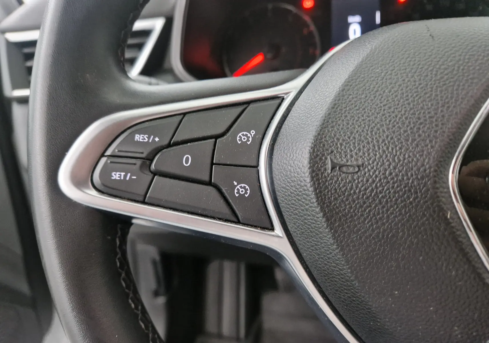 Gros plan sur les commandes de régulateur de vitesse au volant noir d'une Renault Clio V gris platine, 2021.