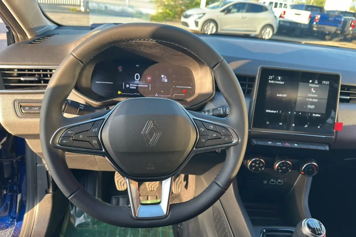 Vue intérieure centrée sur le volant Renault d'une Clio 2025 bleu iron, avec tableau de bord numérique et écran tactile.