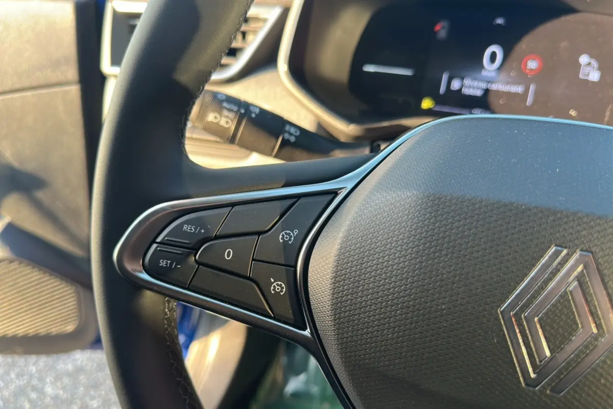 Gros plan sur le volant gauche de la Renault Clio DCI 100 Evolution Camera 2025 bleu iron, avec commandes de régulateur de vitesse.
