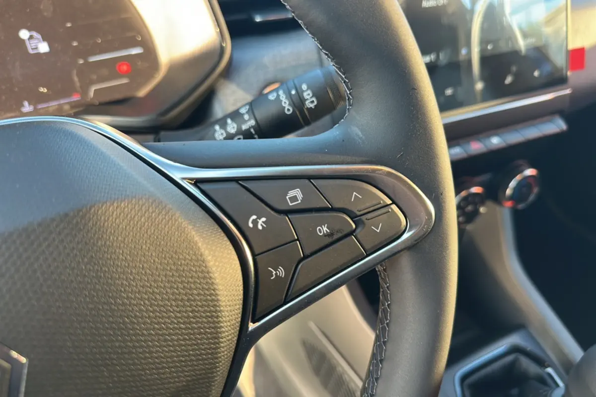 Gros plan sur les commandes du volant d’une Renault Clio 2025, finition DCI 100 Evolution Camera, intérieur noir.