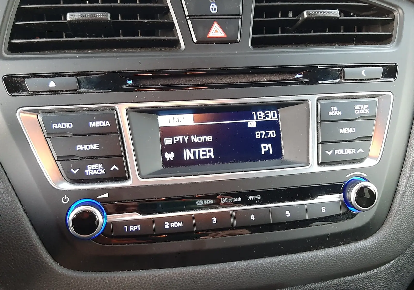 Tableau de bord de Hyundai i20 blanc, vue centrée sur la radio affichant la station INTER 97.7 FM à 18h30.