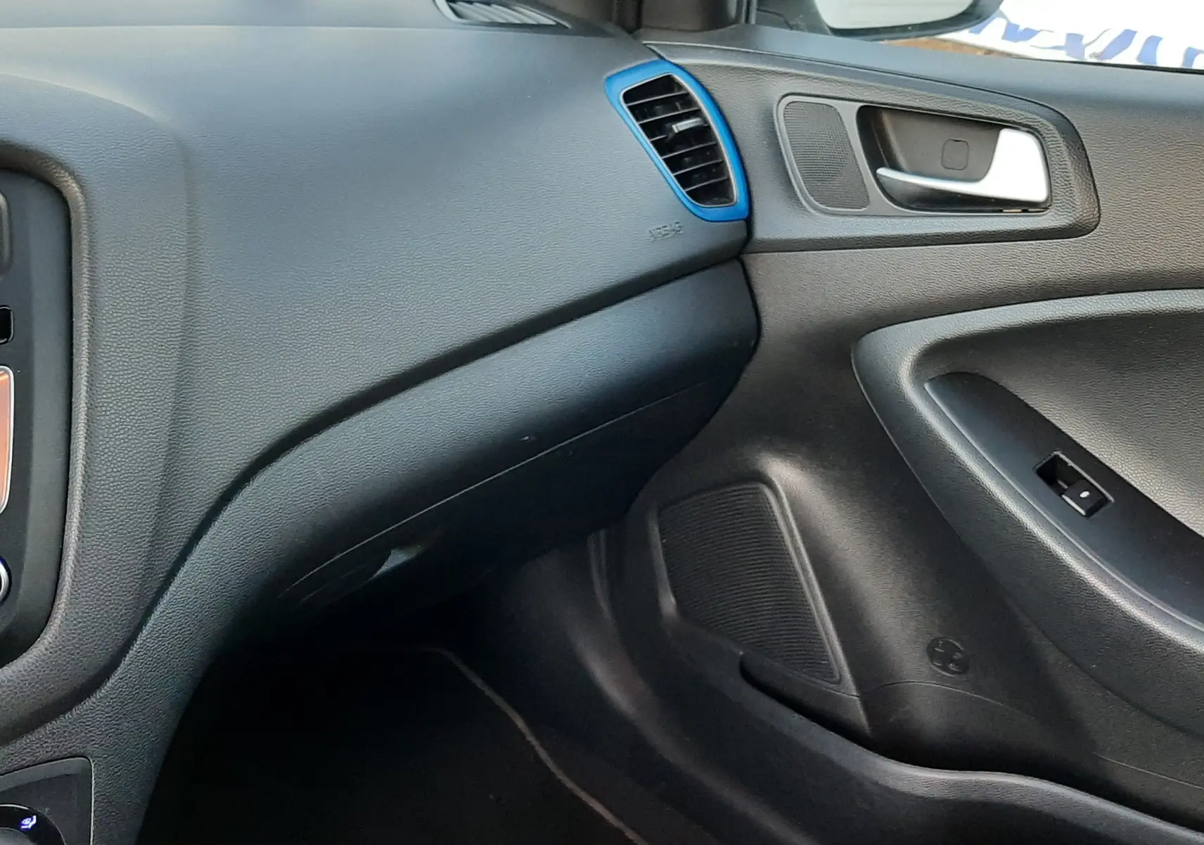 Vue intérieure côté passager de la Hyundai i20 blanche, tableau de bord noir avec aérateurs soulignés de bleu.