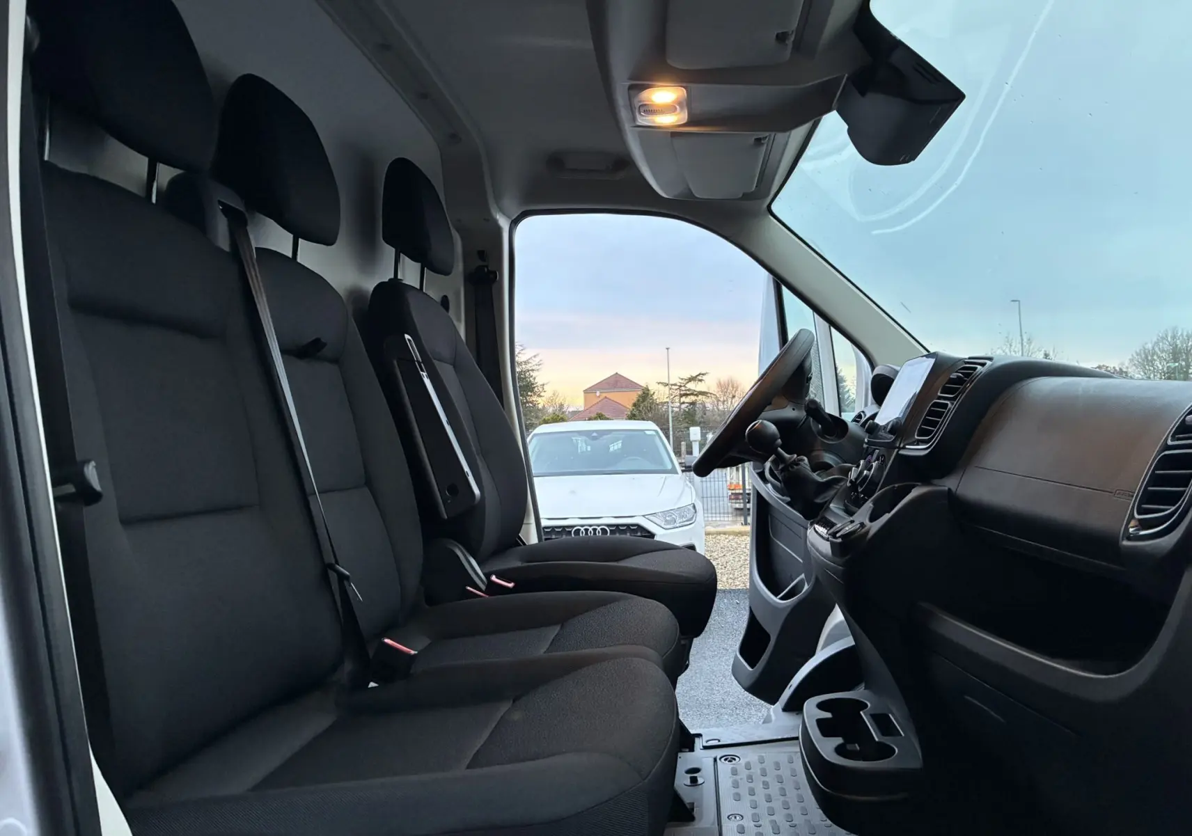 Vue intérieure côté conducteur du Fiat Ducato Fourgon blanc 2025, montrant les sièges noirs en tissu et le tableau de bord.
