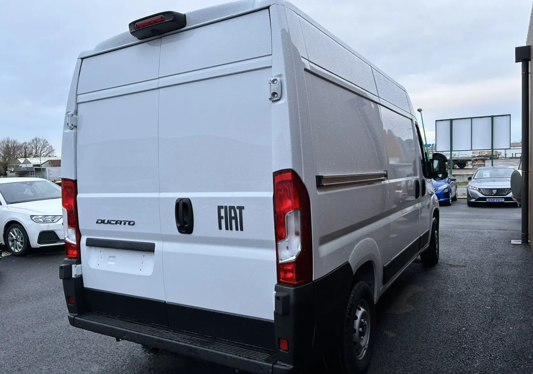 Vue 3/4 arrière droite d’un fourgon blanc Fiat Ducato 2.2 140 L2H2 avec portes arrière fermées sous ciel couvert.