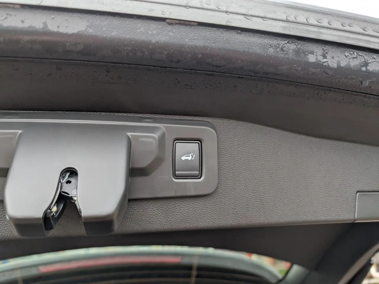 Gros plan sur le bouton d'ouverture motorisée du hayon intérieur d'un Renault Austral gris.