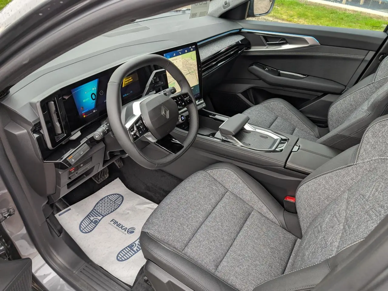 Vue intérieure côté conducteur du Renault Austral gris, mettant en valeur le tableau de bord numérique et les sièges tissu gris clair.