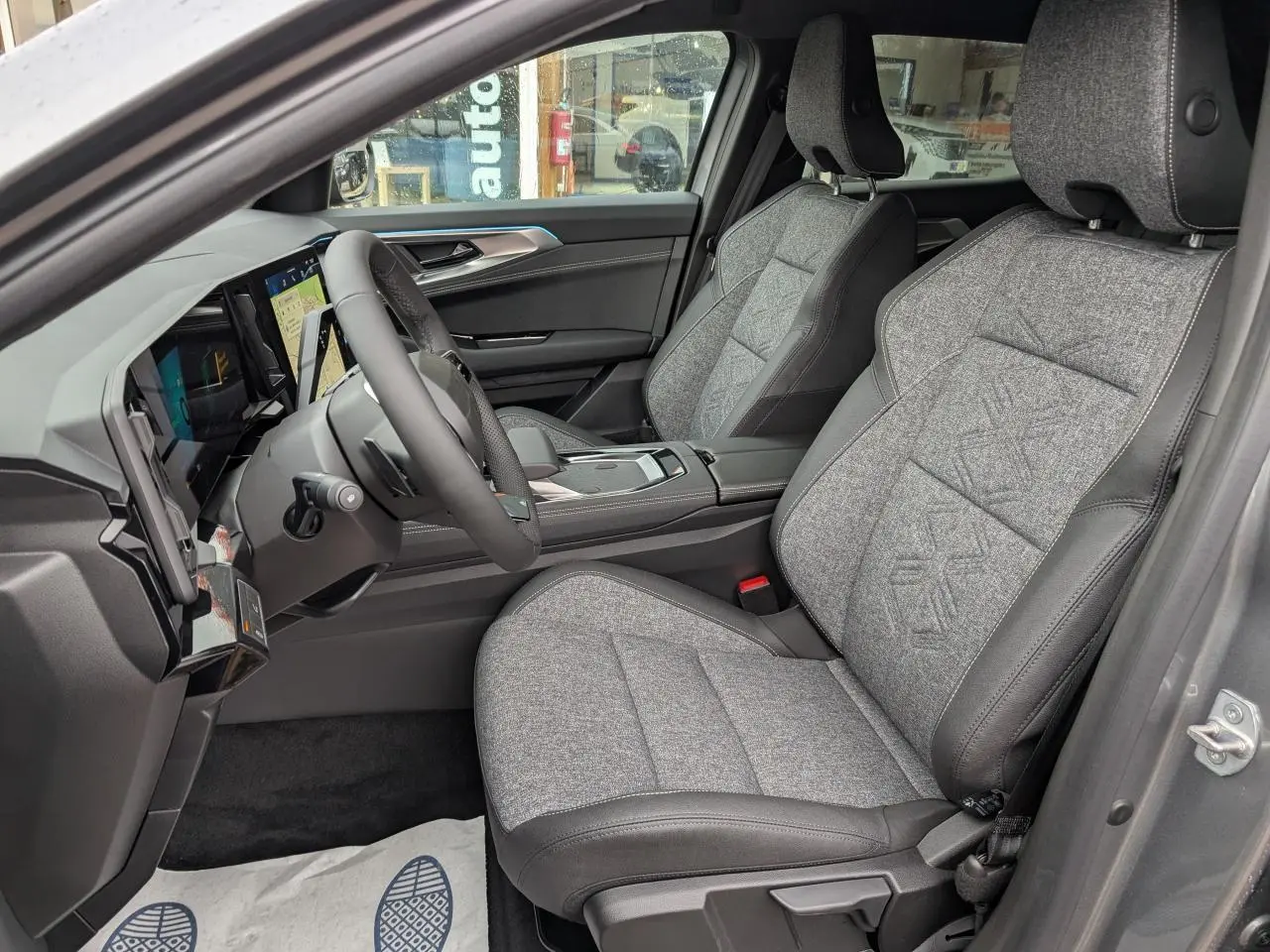 Vue intérieure côté conducteur du Renault Austral 2025, sièges gris clair avec motifs embossés et tableau de bord moderne.