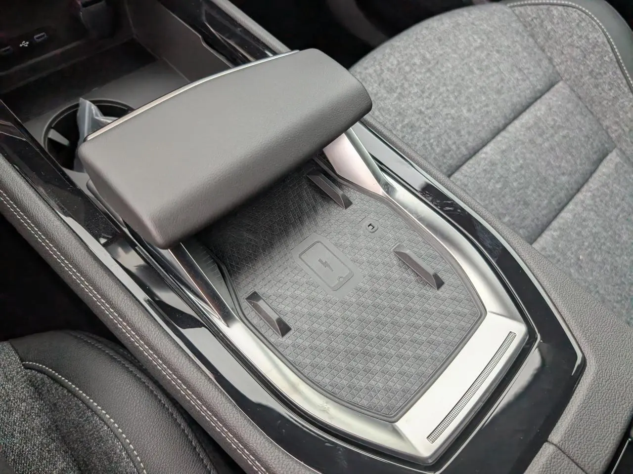 Gros plan sur la console centrale noire avec chargeur à induction et accoudoir, sièges tissu gris clair Renault Austral 2025.