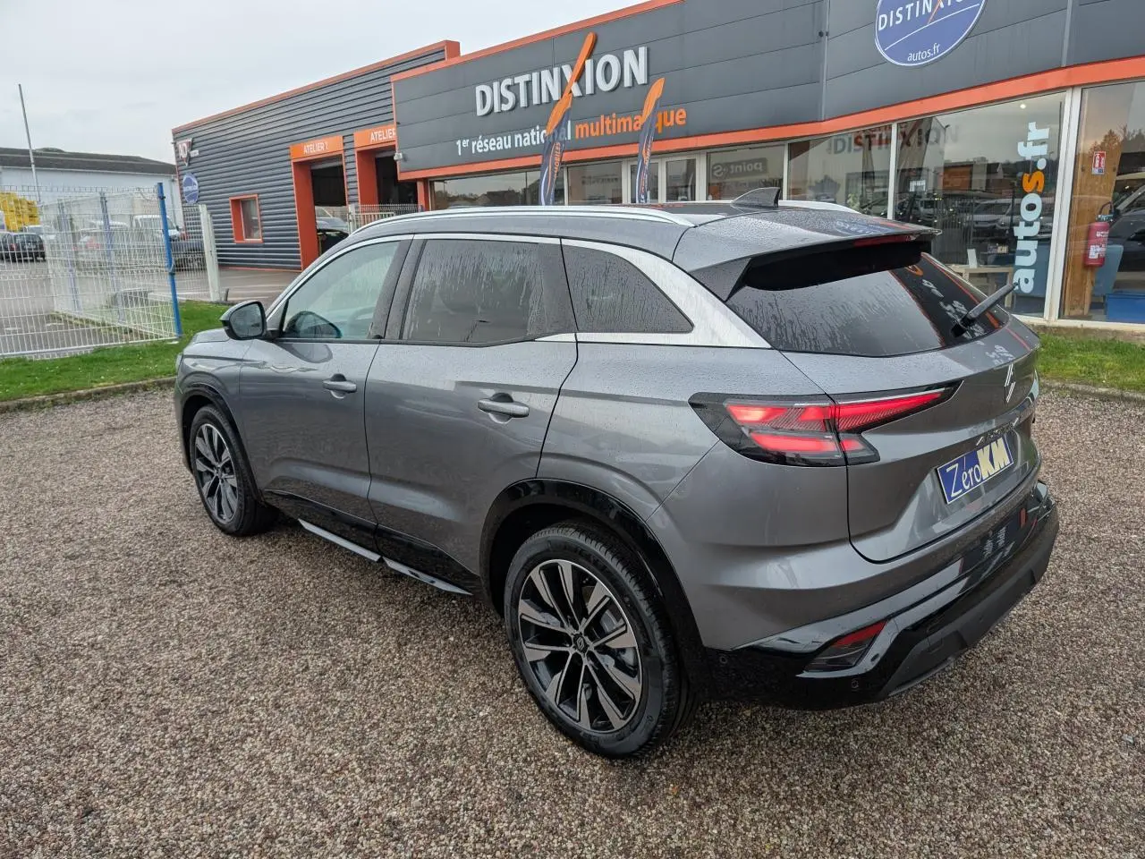 Vue 3/4 arrière droit du Renault Austral gris avec jantes alliage noires et toit noir, stationné devant un showroom Distinxion.