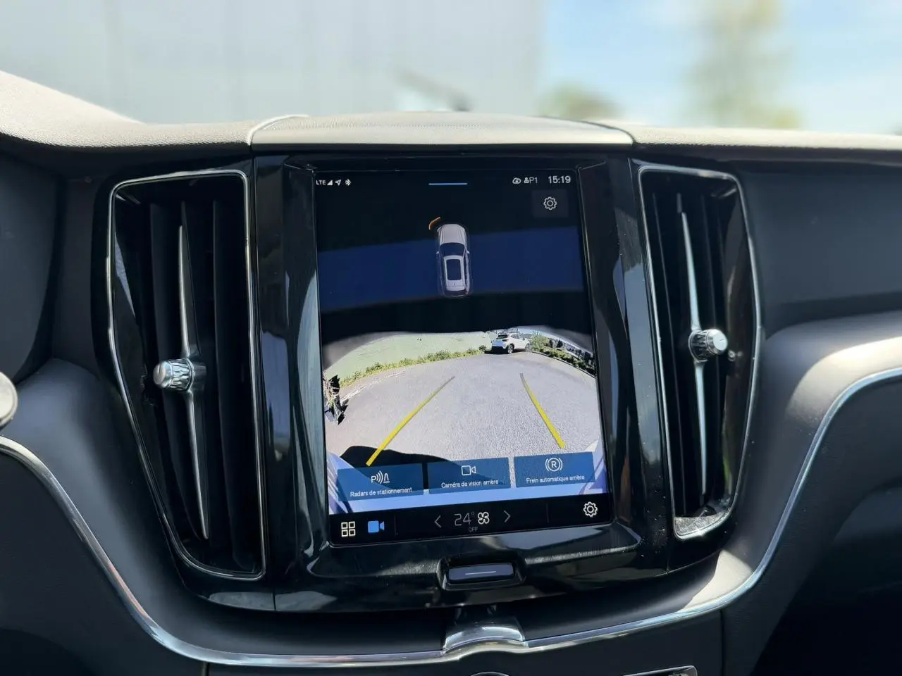 Écran tactile central du tableau de bord du Volvo XC60 blanc, affichant la caméra de recul avec lignes de guidage jaunes.