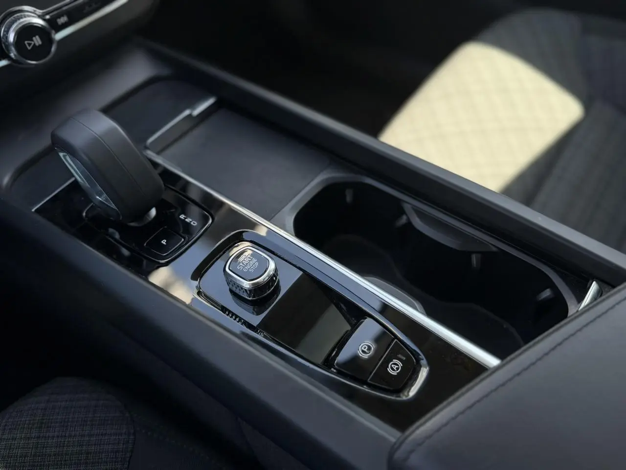 Gros plan sur la console centrale noire du Volvo XC60 blanc, avec levier de vitesse et bouton Start/Stop.