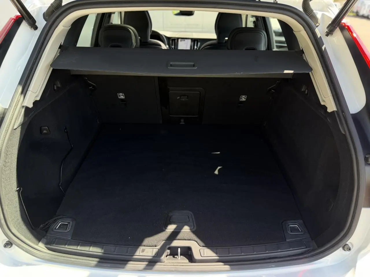 Coffre ouvert vu de l'arrière d'un Volvo XC60 blanc Crystal 2024 avec cache-bagages noir.