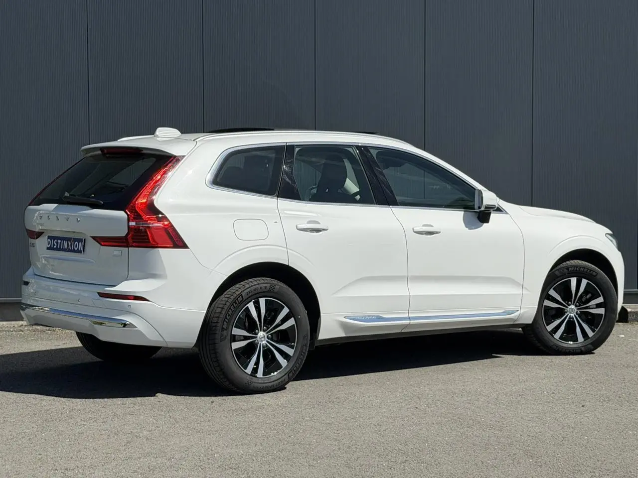 Vue 3/4 arrière droite du Volvo XC60 blanc Crystal avec jantes alliage noires et chrome autour des vitres.
