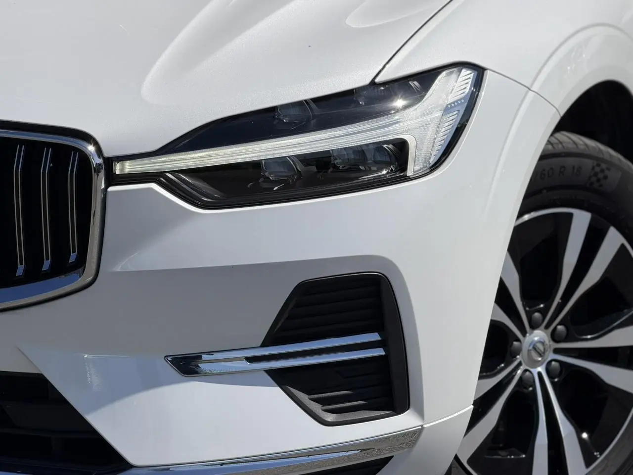 Gros plan sur l'avant droit du Volvo XC60 blanc Crystal, mettant en valeur le phare LED et la jante alliage noire et argent.