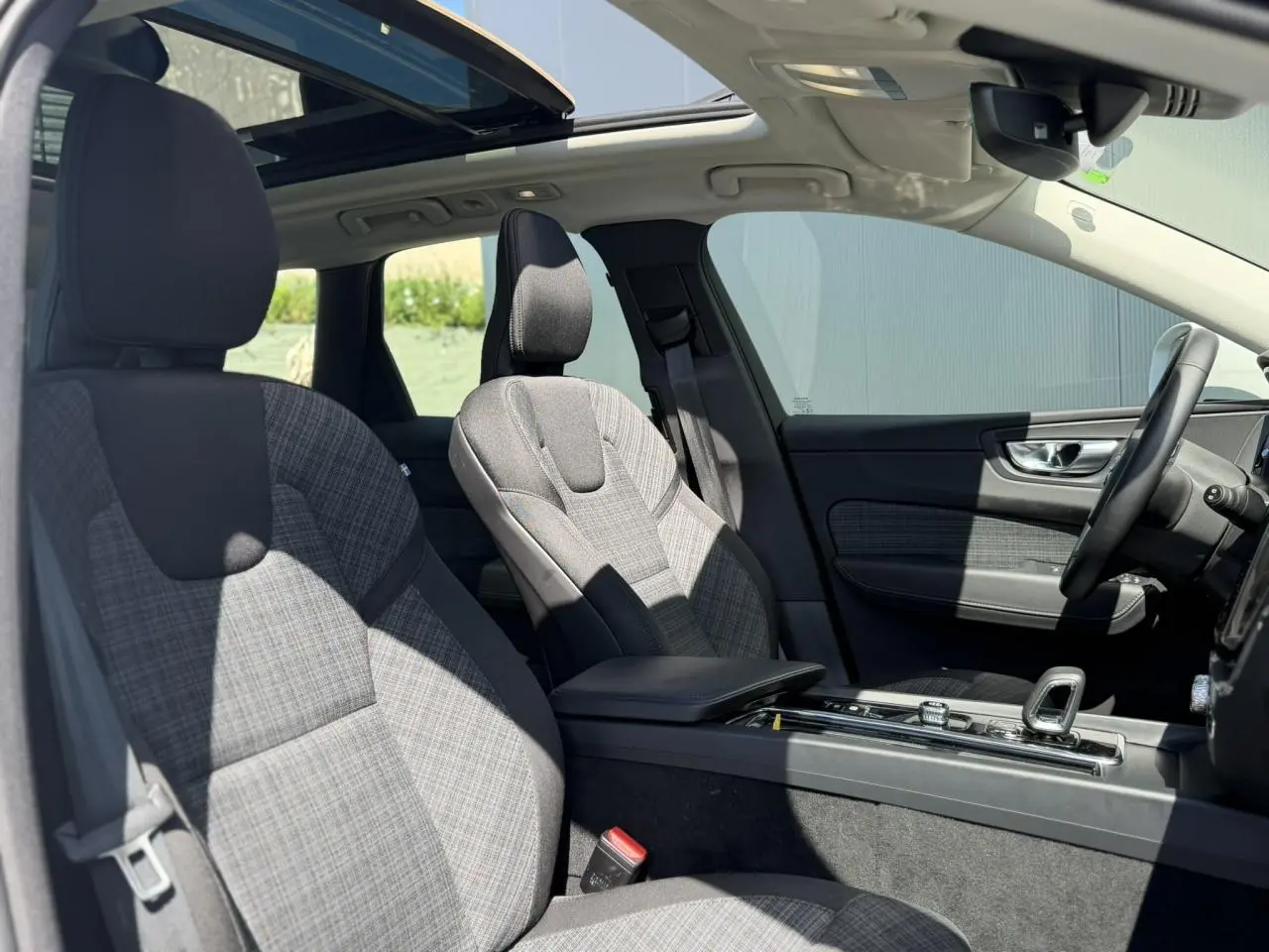 Vue intérieure côté droit du Volvo XC60 2024 T6 AWD PHEV, sièges tissu gris et toit ouvrant panoramique visible.