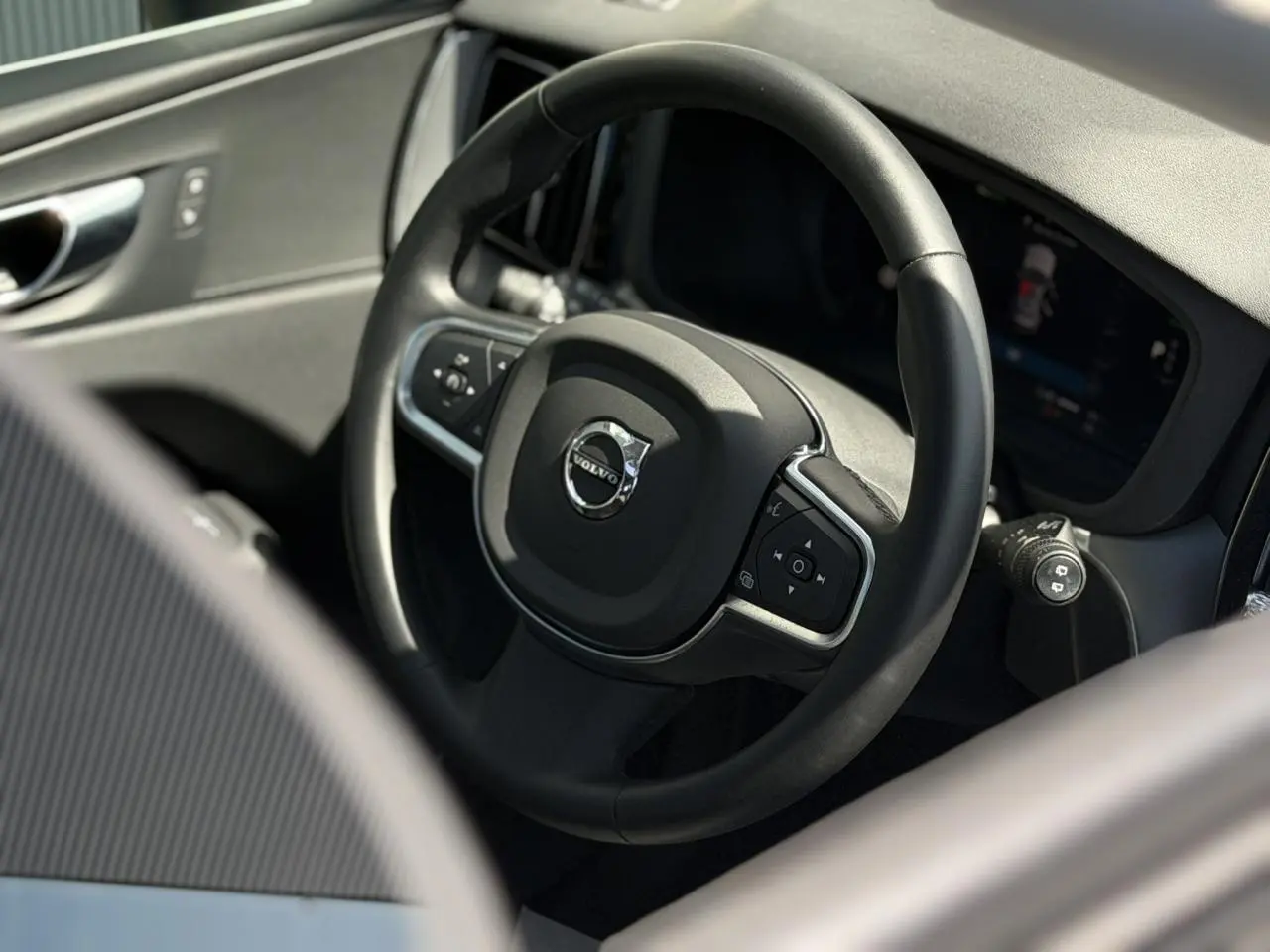 Gros plan sur le volant noir simili-cuir du Volvo XC60 2024, avec commandes intégrées et tableau de bord digital.