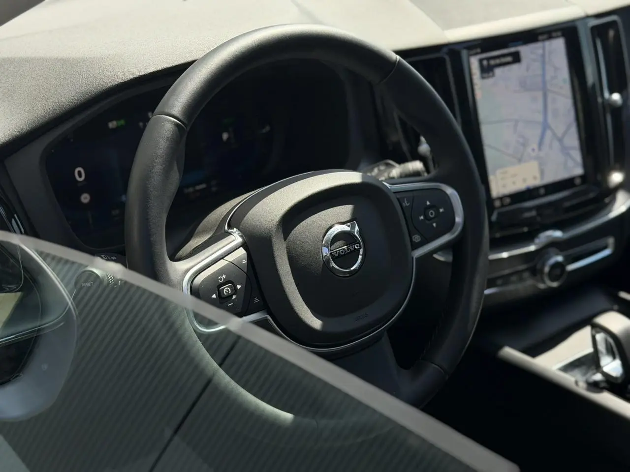 Vue rapprochée du volant noir en simili-cuir du Volvo XC60 2024 avec écran tactile et tableau de bord digital.