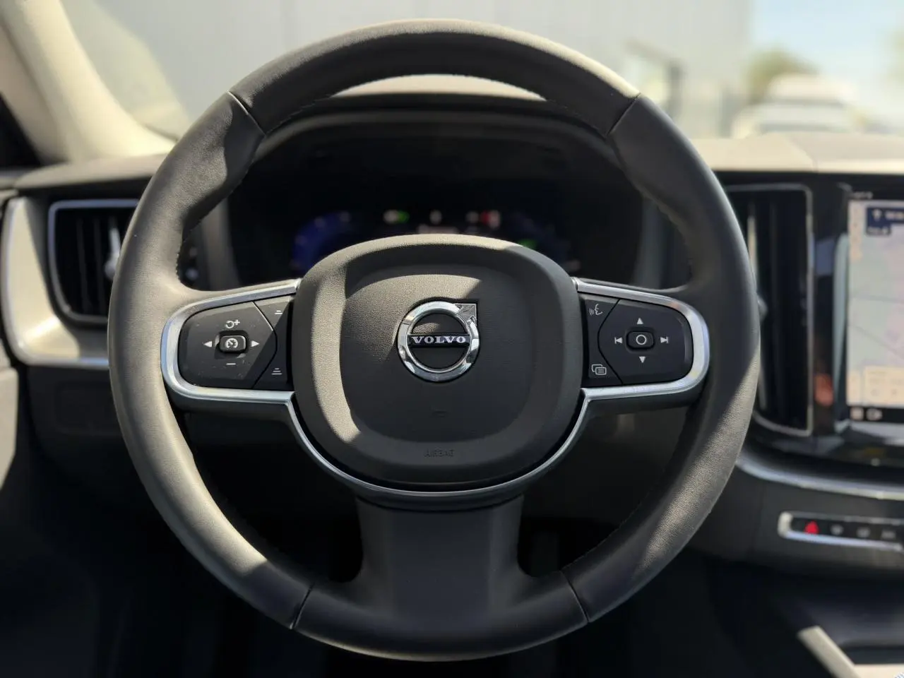 Volant 3 branches en simili-cuir noir de Volvo XC60 T6 AWD PHEV 2024, avec tableau de bord digital et écran tactile visible.