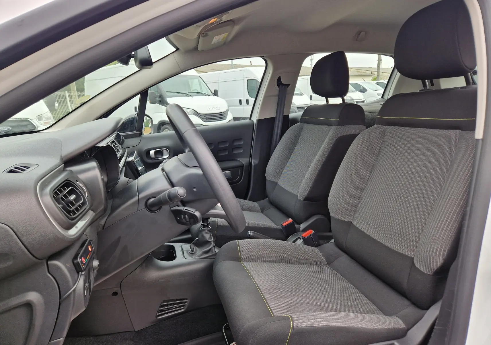 Vue intérieure côté conducteur de la Citroën C3 Société blanche, montrant les sièges gris et la console avec boîte manuelle.