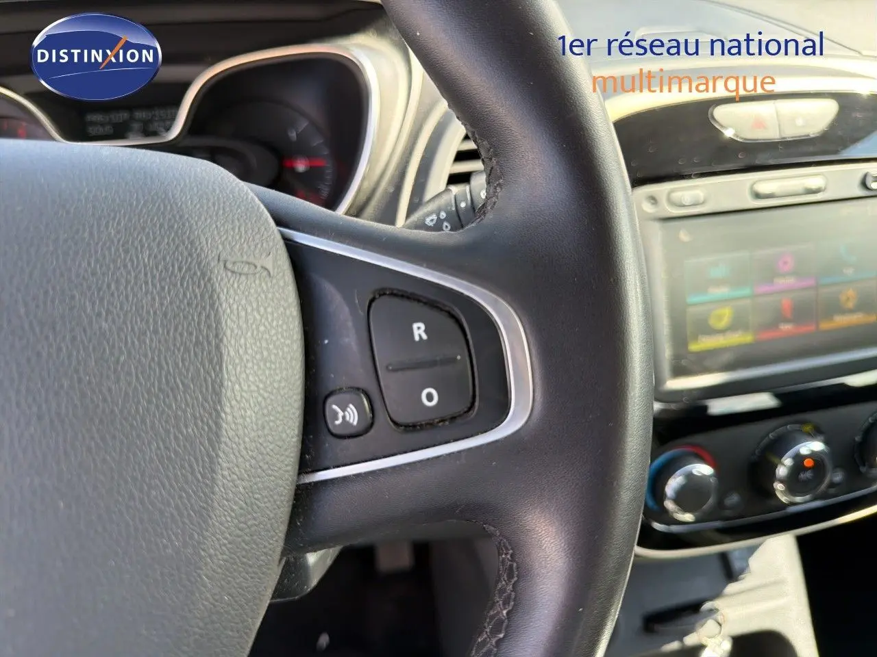 Gros plan sur le volant noir du Renault Captur gris Cassiopée, avec commandes audio visibles et tableau de bord en arrière-plan flou.