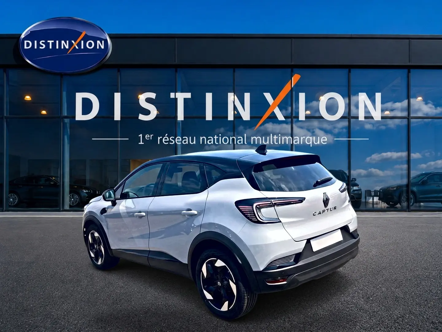 Vue 3/4 arrière droite d'un Renault Captur 1.2 TCe 115 Techno blanc Rafale avec toit noir devant un showroom Distinxion.