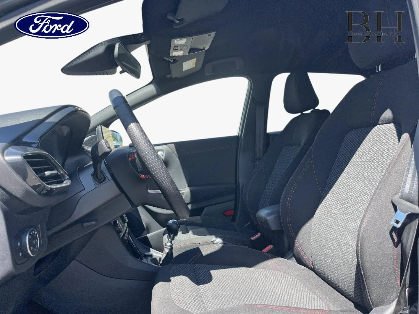 Vue intérieure côté conducteur du Ford Puma 2024, montrant les sièges en tissu noir avec surpiqûres rouges et la boîte manuelle.