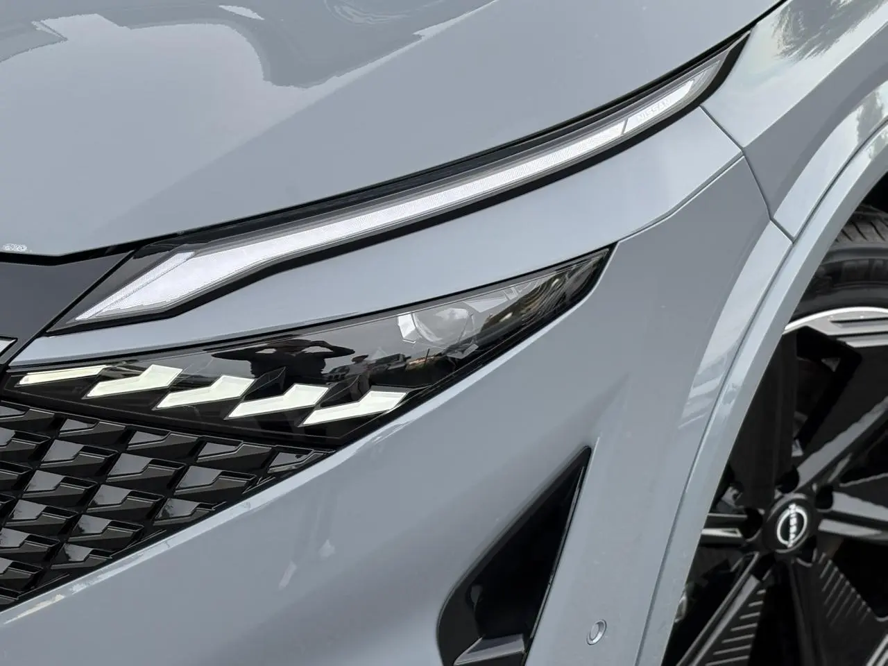Gros plan sur le phare avant droit du Nissan Qashqai gris Ceramic avec calandre noire et jante alliage 20 pouces.