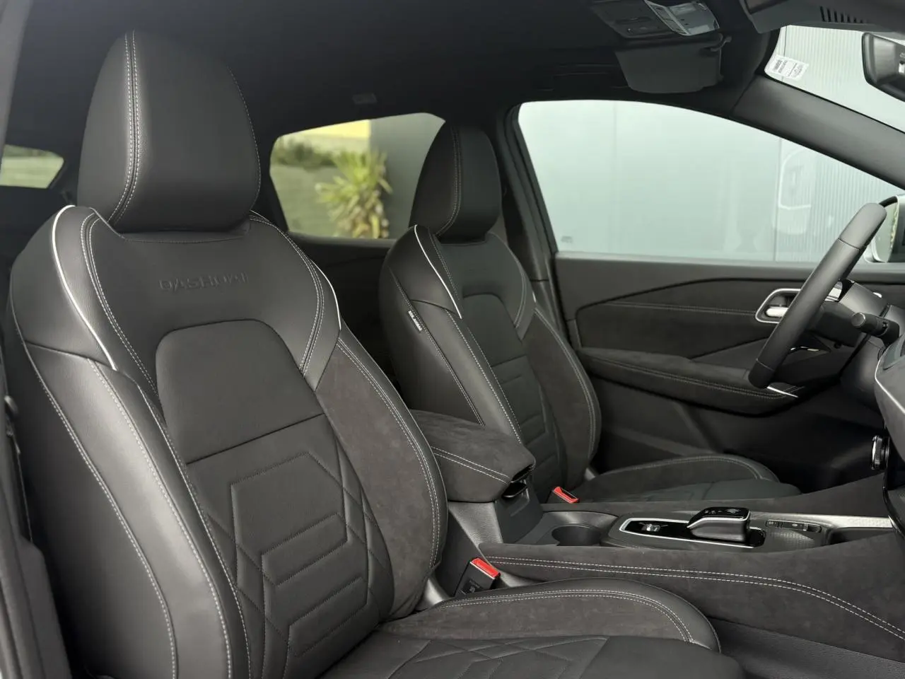 Intérieur du Nissan Qashqai 2025, vue côté conducteur, sièges Alcantara et cuir noirs avec surpiqûres blanches.