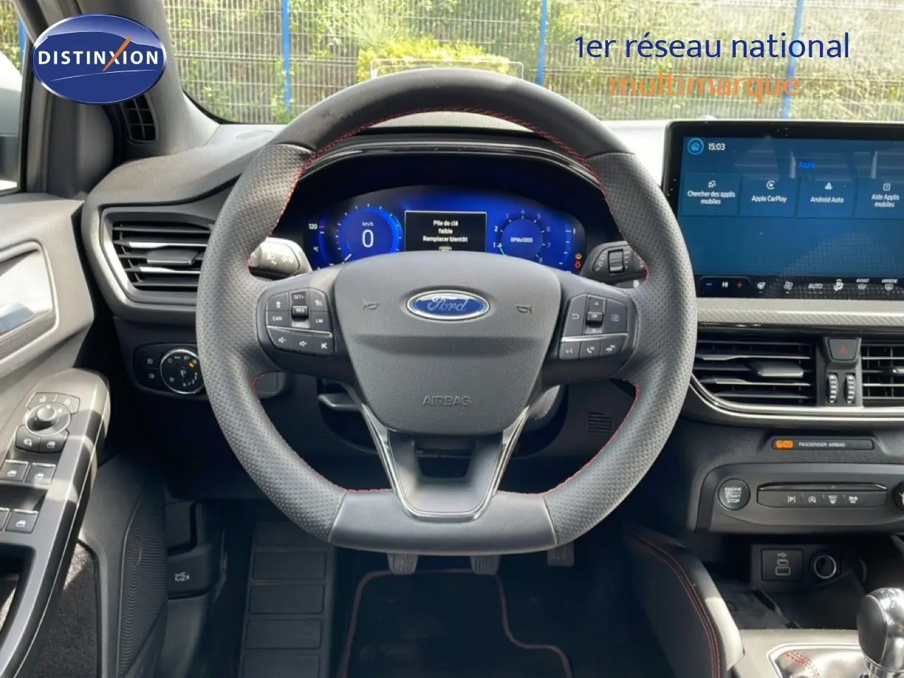 Vue intérieure centrée sur le volant perforé avec coutures rouges et tableau de bord numérique de la Ford Focus SW 2023.