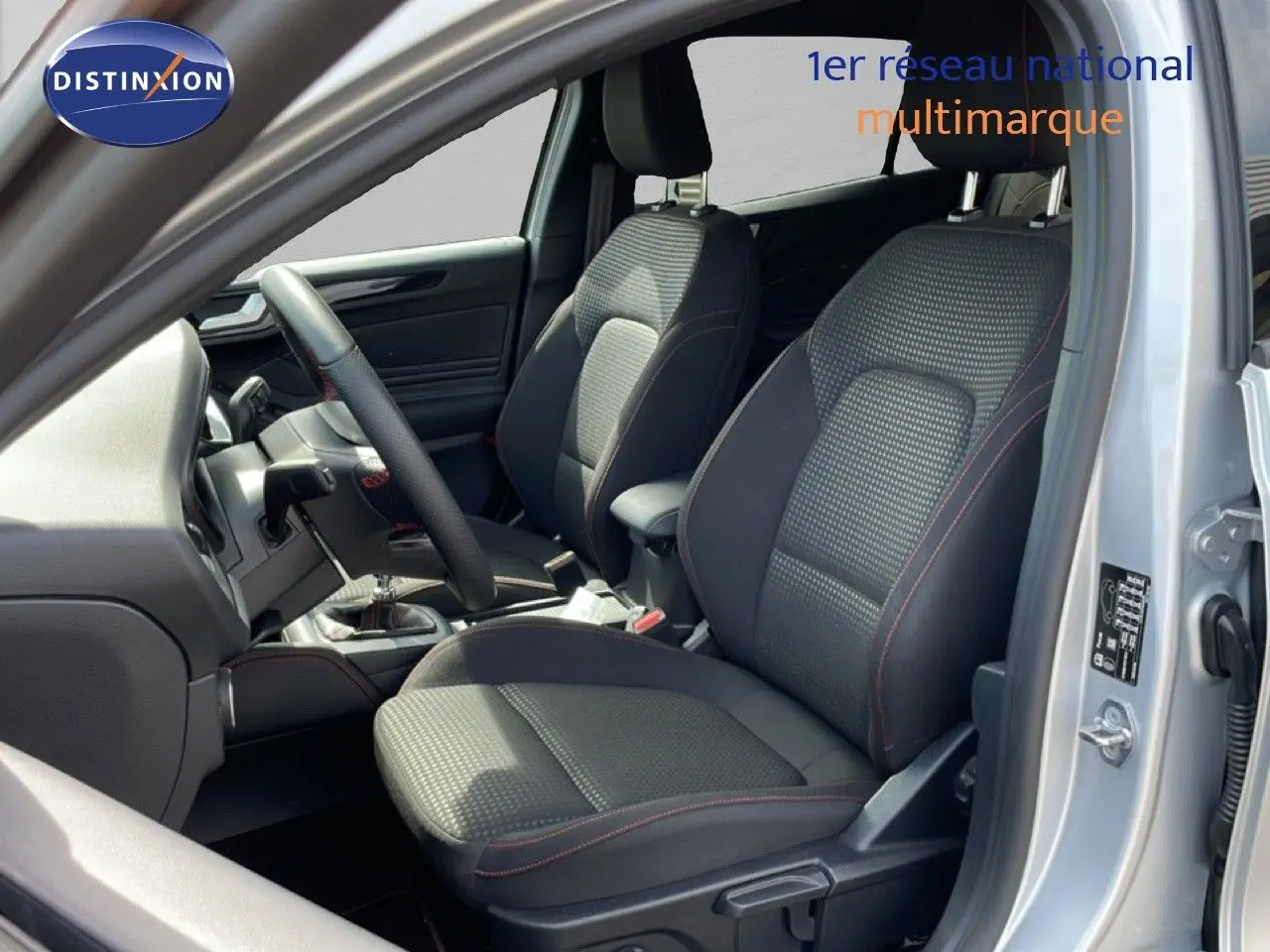 Vue intérieure côté conducteur de la Ford Focus SW gris lunaire, sièges tissu noir avec surpiqûres rouges et volant cuir.