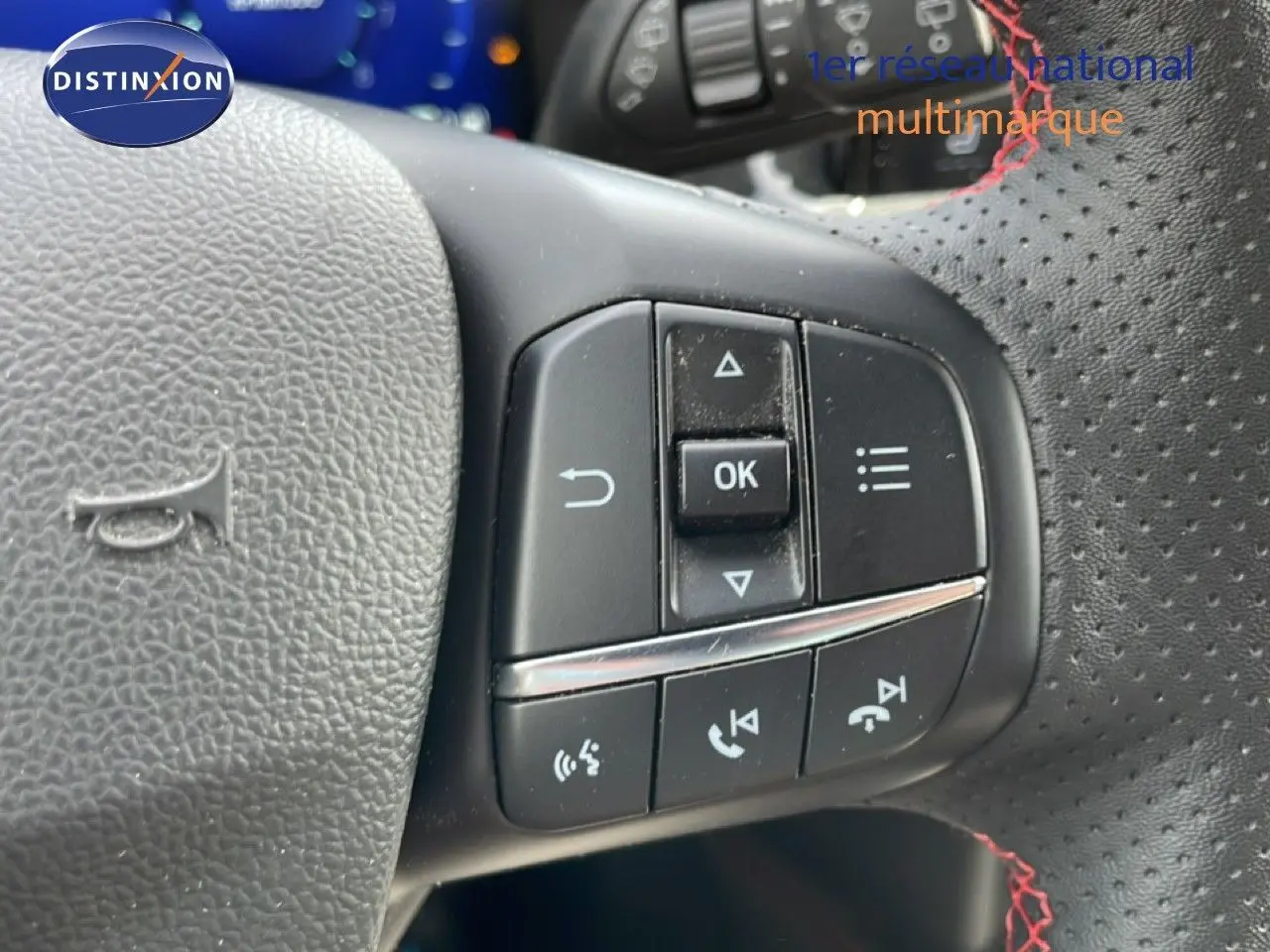 Gros plan sur les commandes multifonctions noires à droite du volant perforé avec surpiqûres rouges d’une Ford Focus SW 2023.