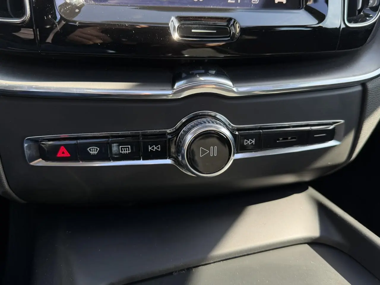 Gros plan sur la commande centrale multimédia noire avec boutons de lecture et alertes du Volvo XC60 gris Dusk 2024.