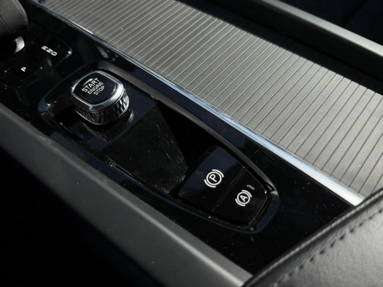 Gros plan sur la console centrale noire du Volvo XC60 T6 AWD PHEV 2024 avec bouton Start/Stop et frein à main électronique.
