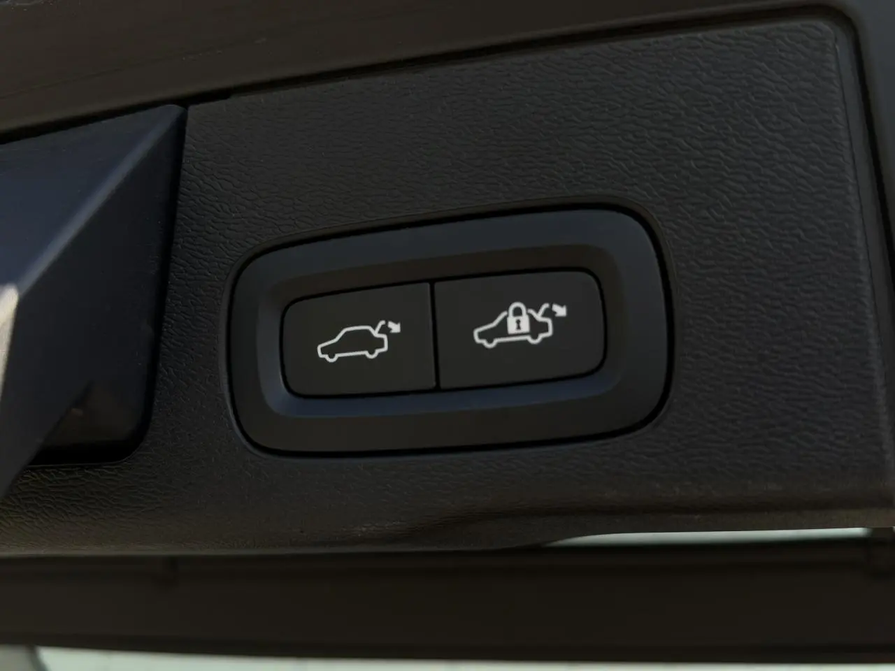 Gros plan sur les boutons d'ouverture et de verrouillage du hayon électrique du Volvo XC60 gris Dusk.