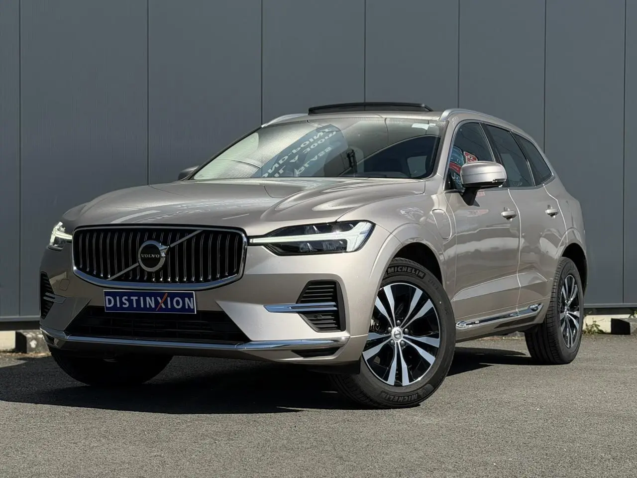 Volvo XC60 T6 AWD PHEV gris Dusk en 3/4 avant droit, avec jantes alliage et contours chromés visibles.