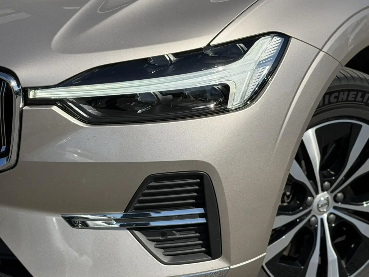 Gros plan sur l'avant droit du Volvo XC60 gris Dusk, mettant en valeur le phare LED et la jante alliage 18 pouces.